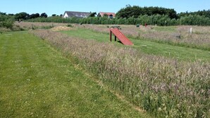 A grassy field with a red slide and picnic table, surrounded by trees and houses in the background. - Holiday Home in FanÃ¸ (Fano)