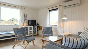 A cozy living room with wicker chairs, a sofa, a TV, and a bookshelf. - Holiday Home in FanÃ¸ (Fano)
