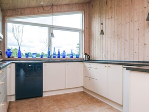 A kitchen with a large window, wooden walls, and a tiled floor. - Holiday Home in Ansager (Ansager)