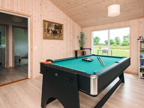 A pool table with a green felt surface, a framed painting on the wall, and a view of the outdoors through a large window. - Holiday Home in Ansager (Ansager)