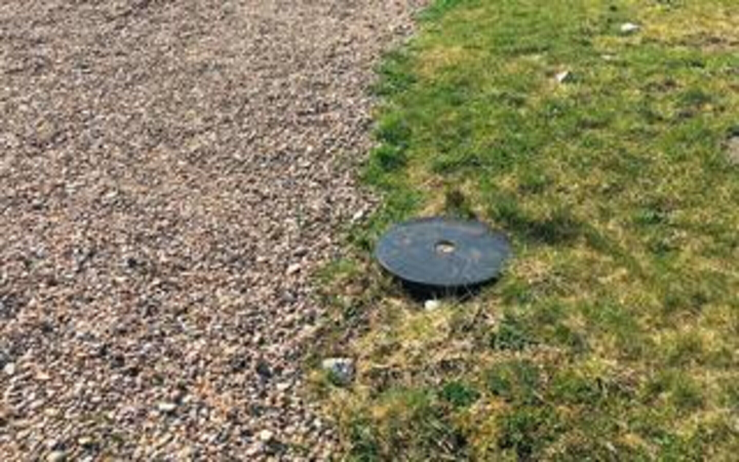 A circular object on a gravel surface with grass nearby.