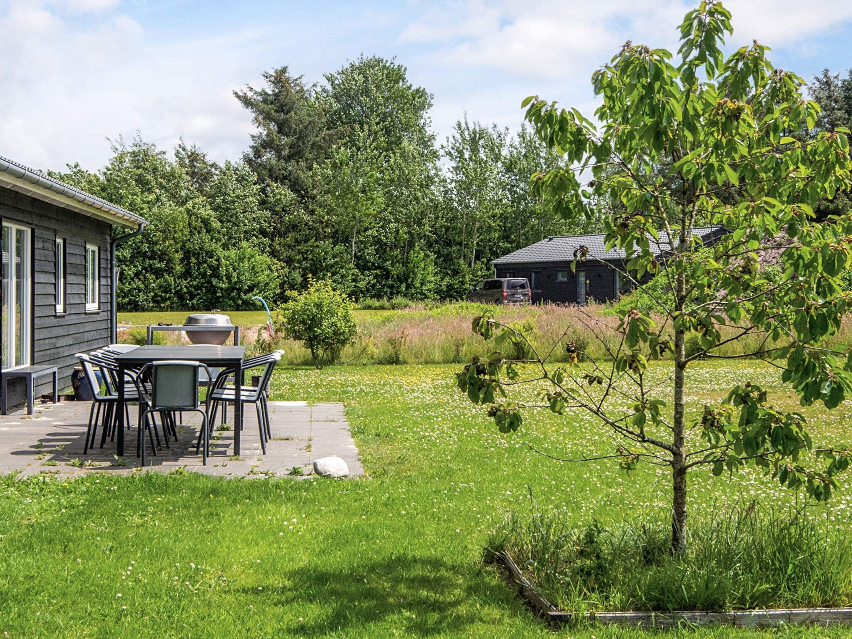 A patio with a table and chairs, a grill, and a small tree.