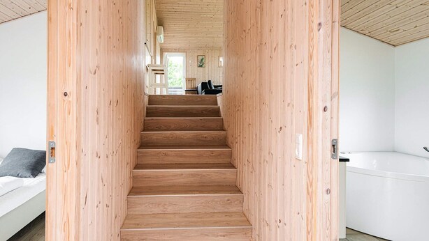 Una escalera de madera conduce a una sala de estar con un sofá y una mesa de comedor.