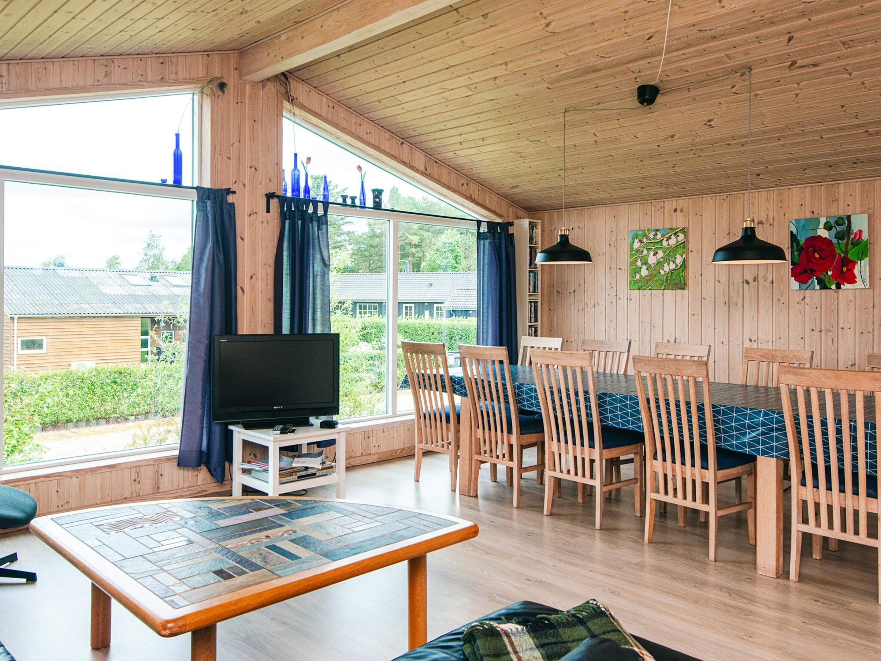 Un intérieur en bois comprenant un coin repas, un téléviseur et de grandes fenêtres.