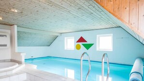 Ein Hallenbad mit schräg laufender Decke, gefliestem Boden und einer Treppe zu einer Whirlwanne.