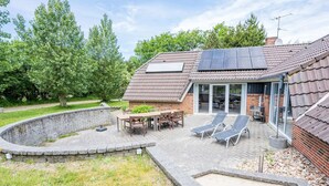 Ein Haus mit Terrasse, einem Tisch, Stühlen und einer Liegewiese.
