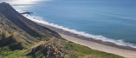A coastal landscape with a beach, grassy slopes, and a clear view of the ocean.