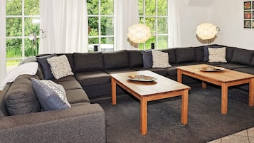 A modern living room with a sectional sofa, two wooden coffee tables, and large windows with curtains.