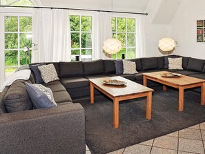Uma sala de estar moderna com sofá seccional, duas mesas de centro de madeira e janelas amplas com cortinas.