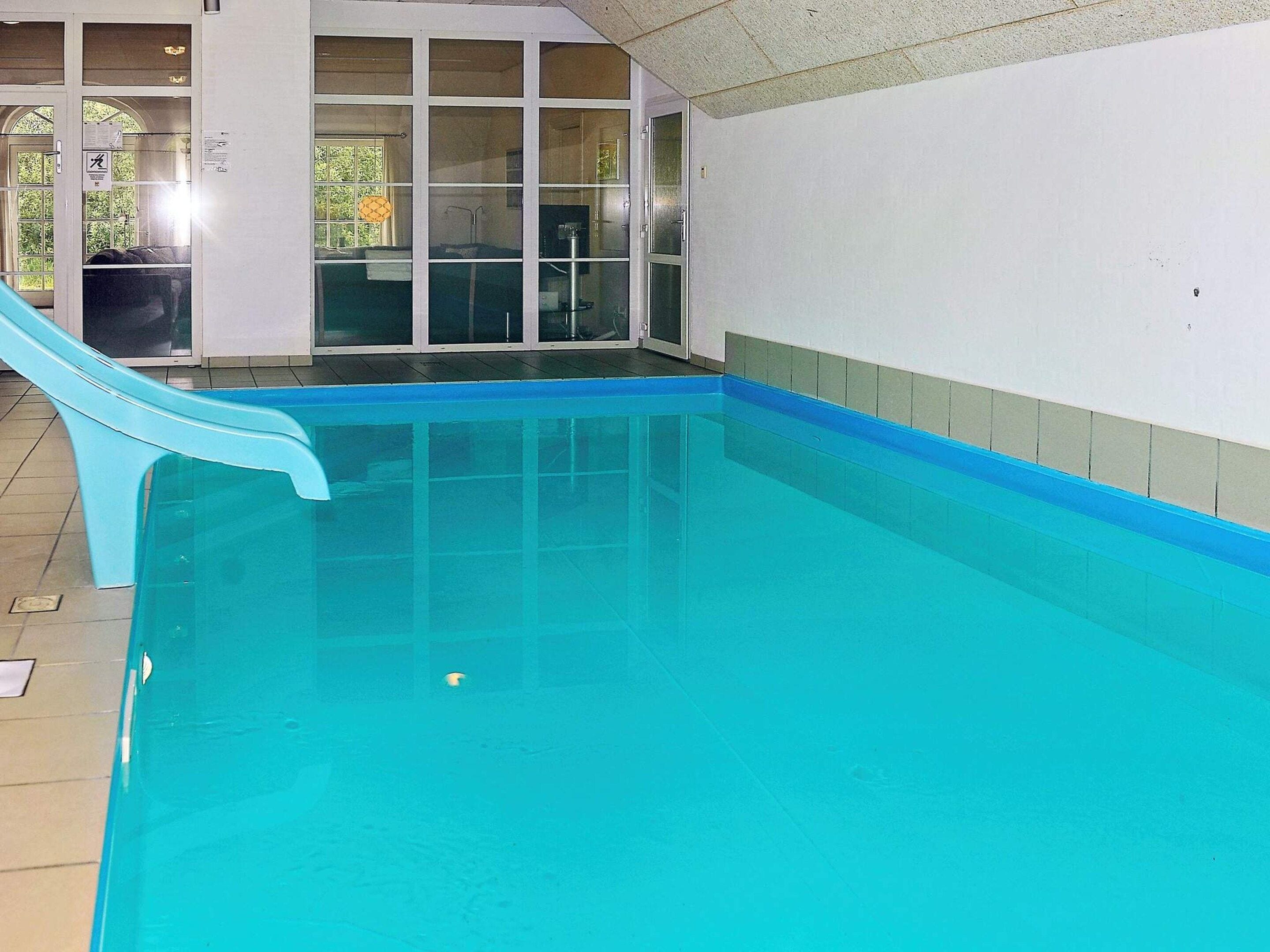 En indendørs swimmingpool med rutsjebane, glasdøre og flisegulv.