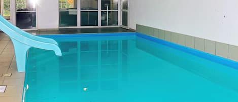 En indendørs swimmingpool med rutsjebane, glasdøre og flisegulv.