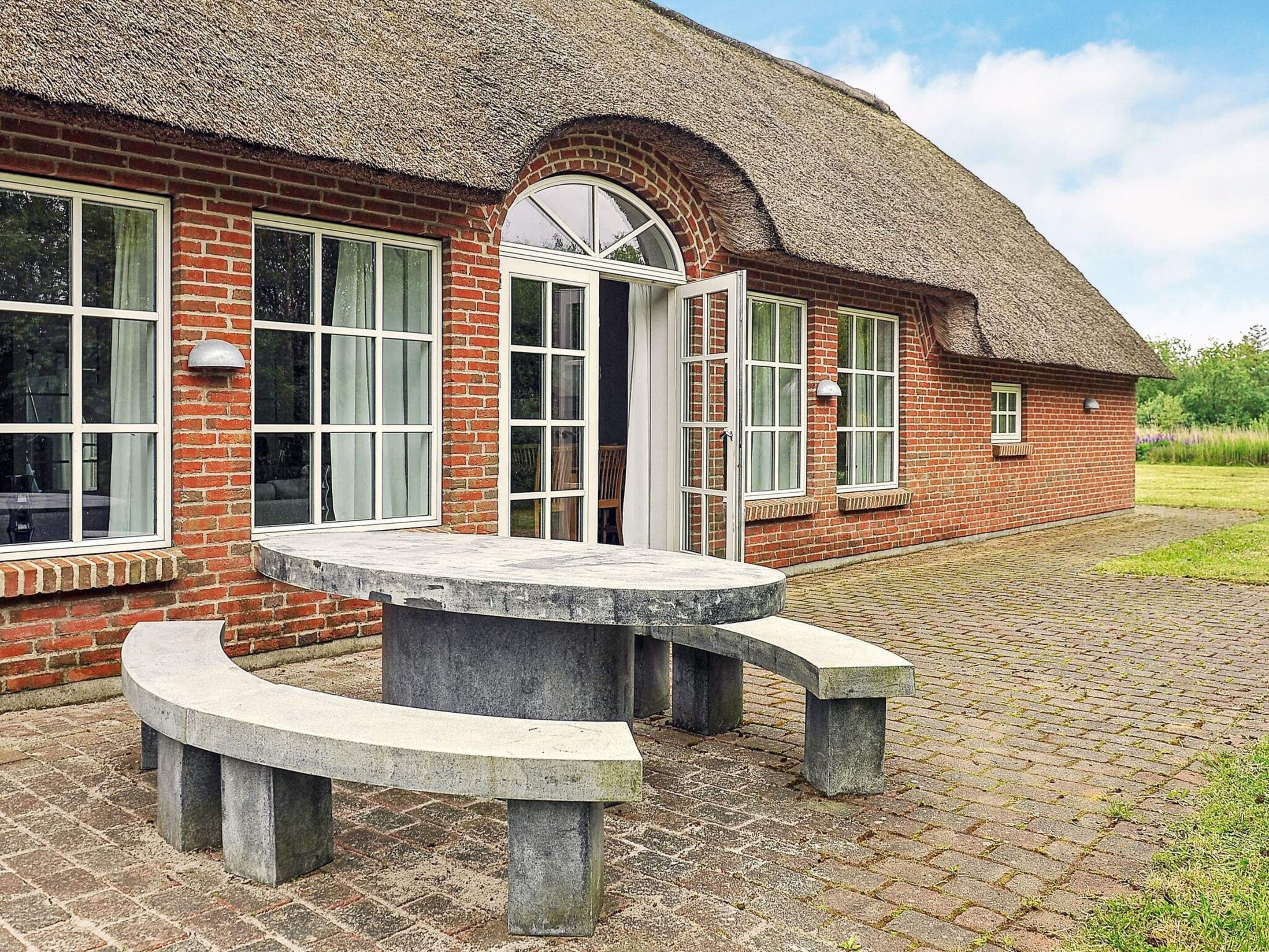 A brick building with a thatched roof, a circular stone bench, and a paved walkway.