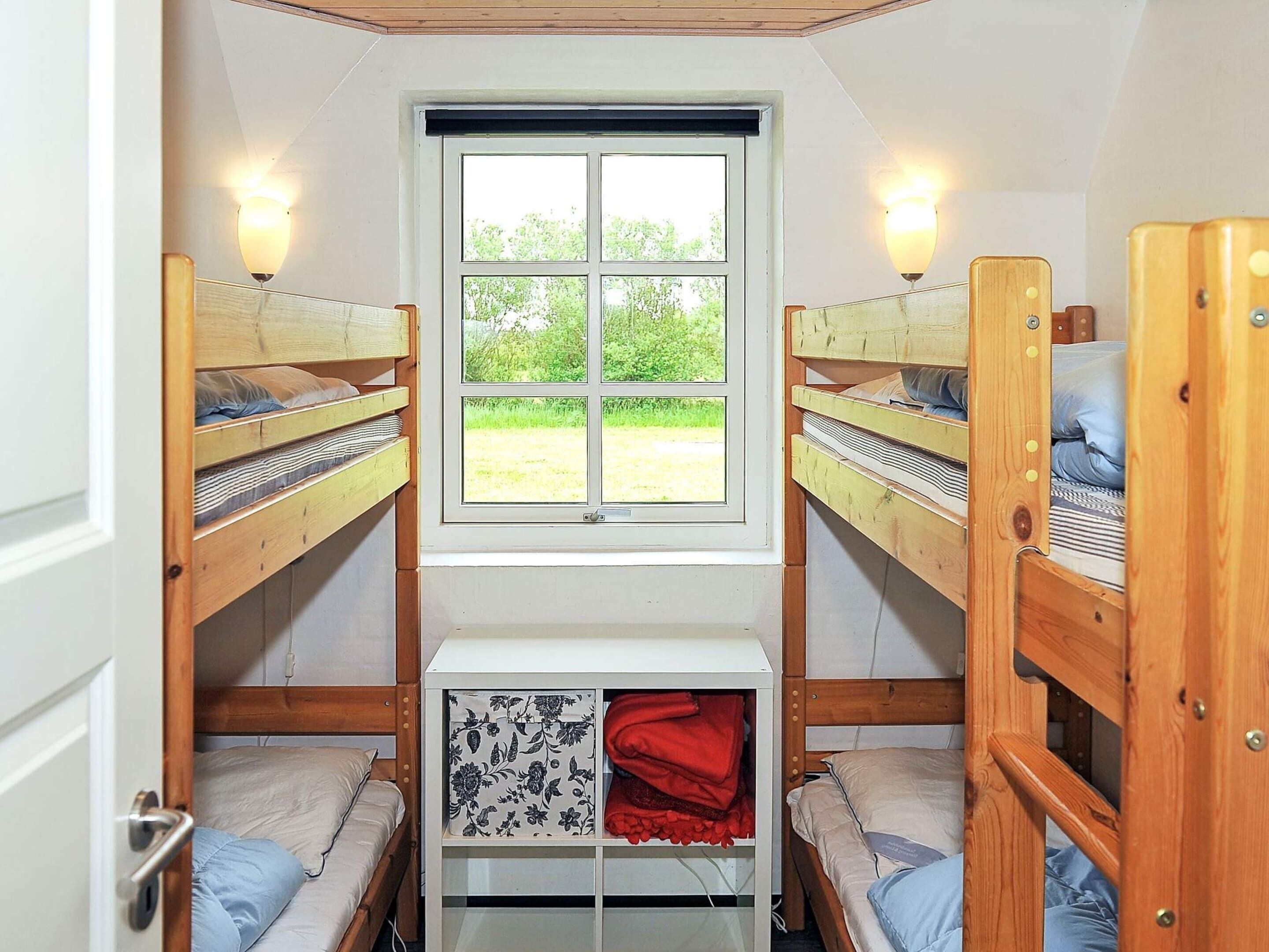 Ein Schlafsaalzimmer mit Etagenbetten, einem Fenster und einem kleinen Stauraum.