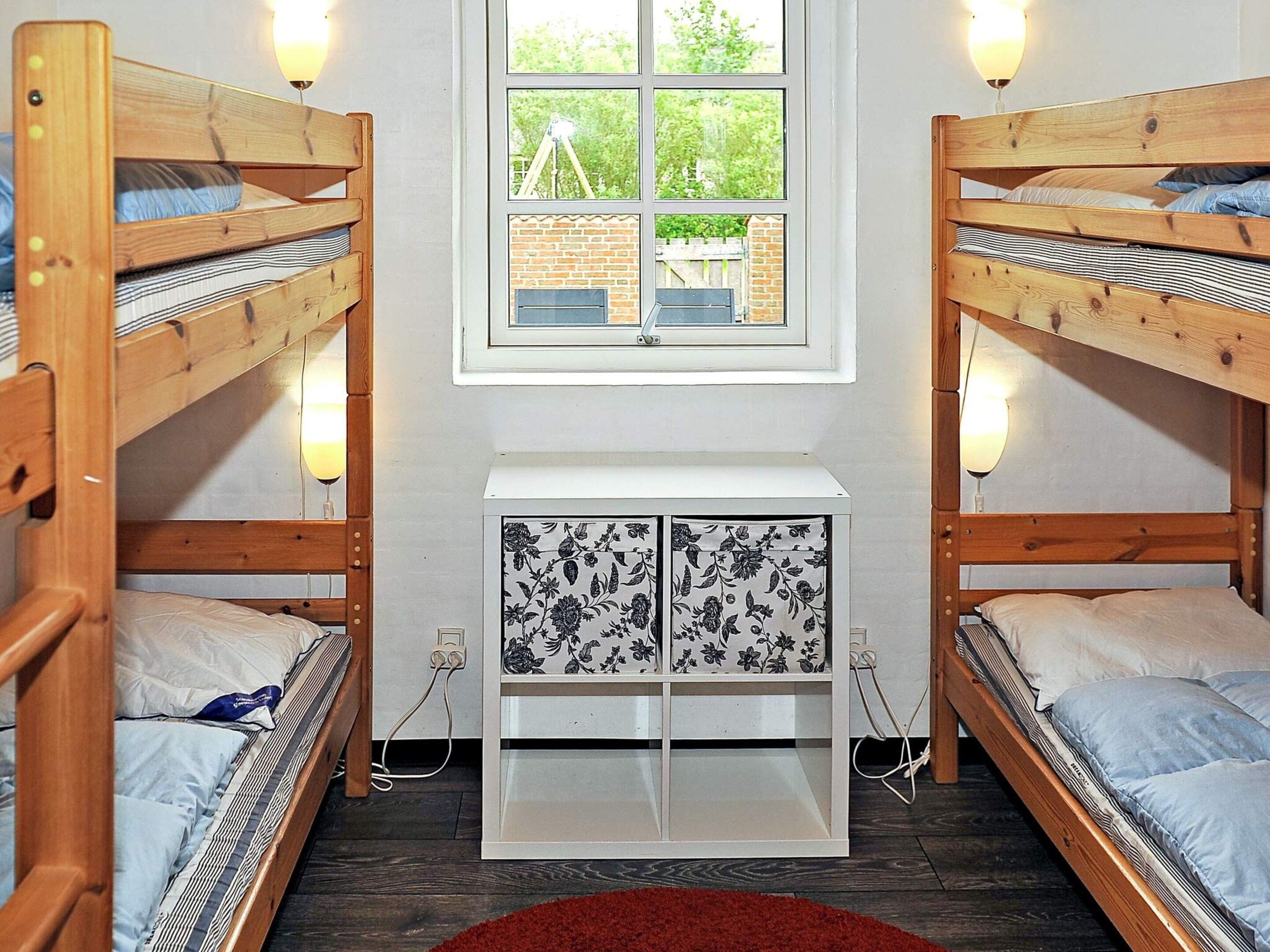 A room with two bunk beds, a small white cabinet with floral patterns, and a window with a view of greenery.