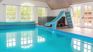 Piscina interna com escorregador, janelas amplas e piso revestido.