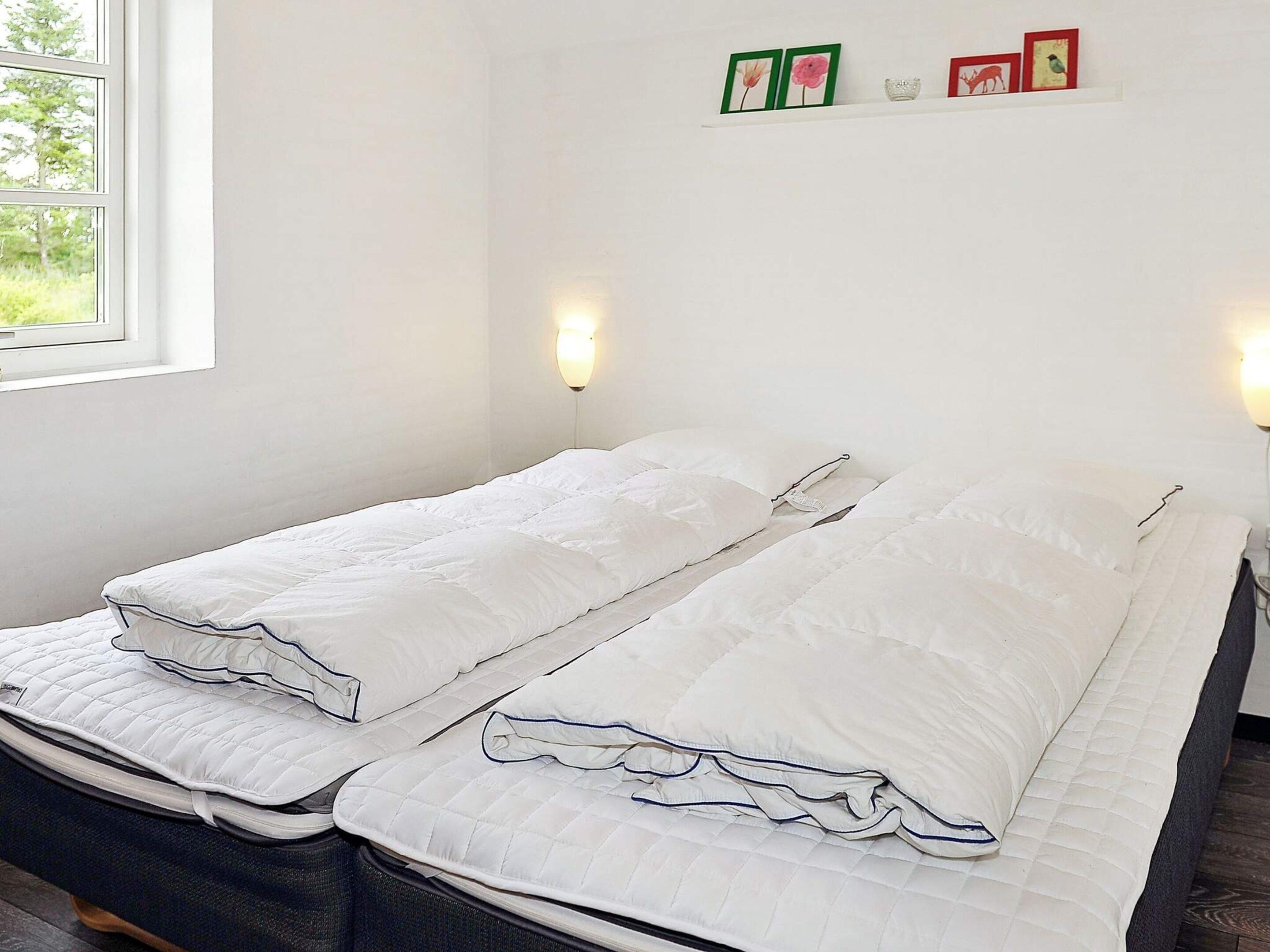 Una cama doble con ropa de cama blanca y un cabecero, una ventana con vistas a árboles y cuadros colgados en la pared.