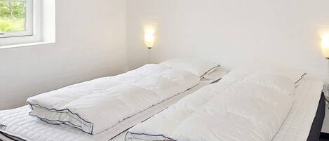 Una cama doble con ropa de cama blanca y un cabecero, una ventana con vistas a árboles y cuadros colgados en la pared.