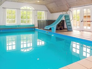 An indoor swimming pool with a slide, large windows, and a tiled floor. - Holiday Home in Ulfborg (Ulfborg)