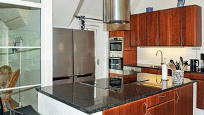 Uma cozinha moderna com eletrodomésticos de aço inoxidável, armários de madeira e uma área de jantar envidraçada.