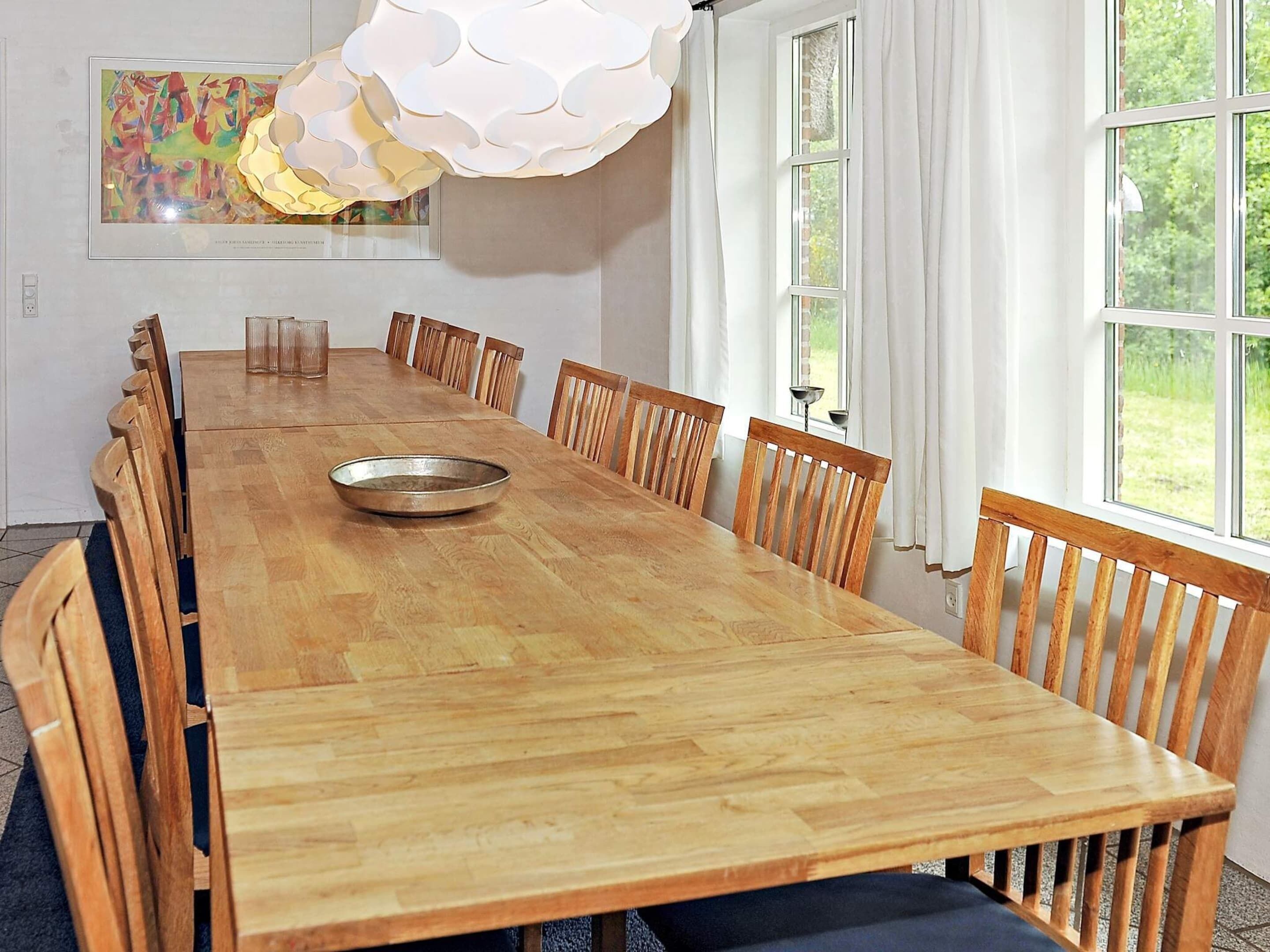 A long wooden dining table with chairs, a metal bowl, and a framed abstract painting on the wall.