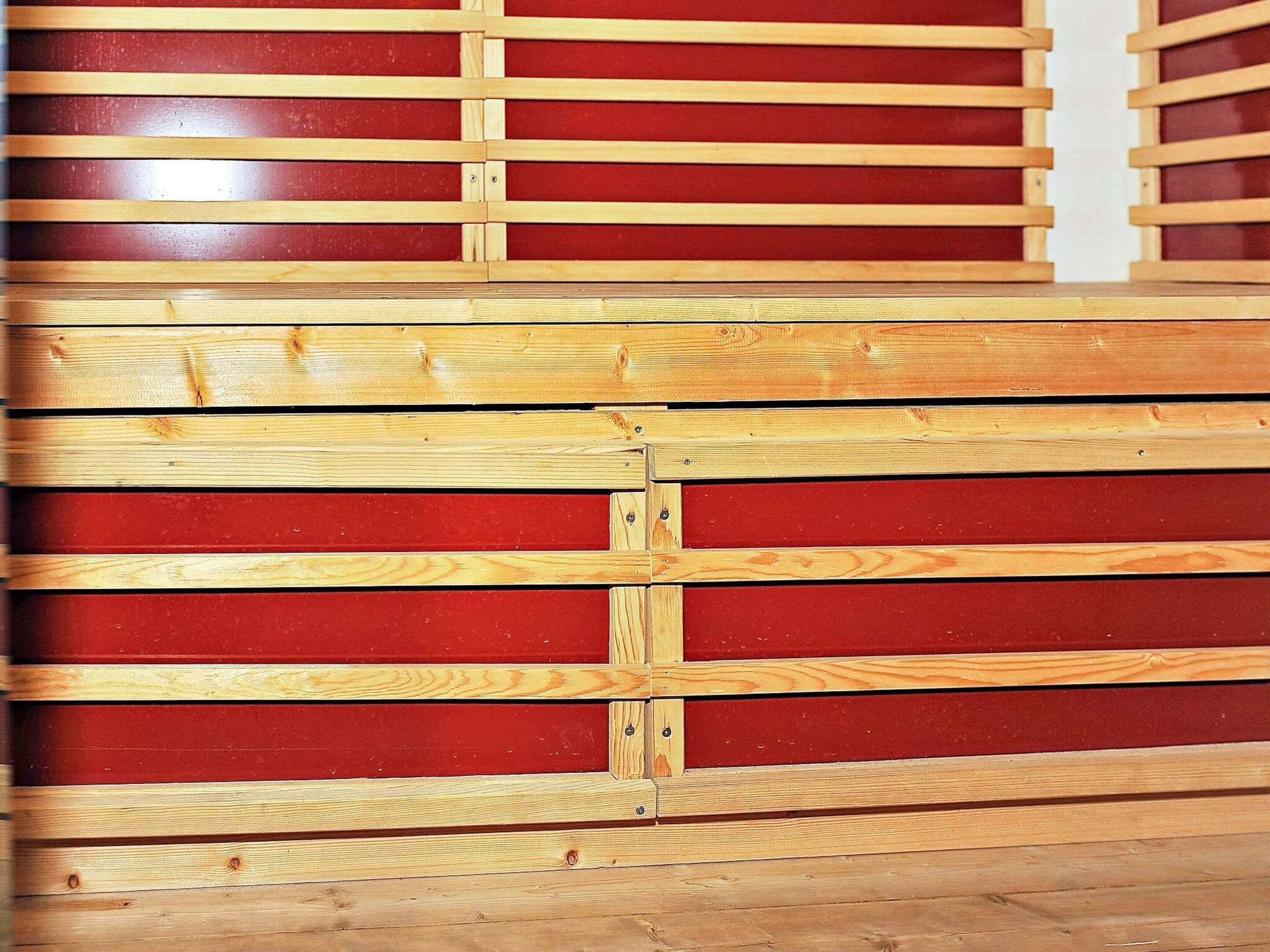 A wooden bench with a red backrest and a wooden floor.