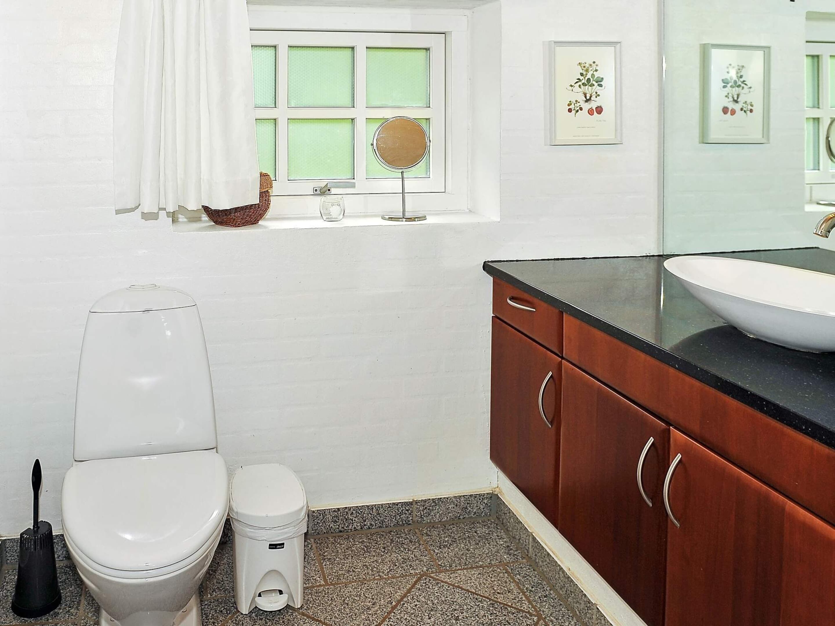 A bathroom with a white toilet, a bidet, a sink with a black countertop, and wooden cabinets.