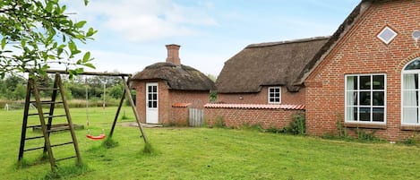 A traditional brick house with a thatched roof, a swing set, and a well-maintained lawn.