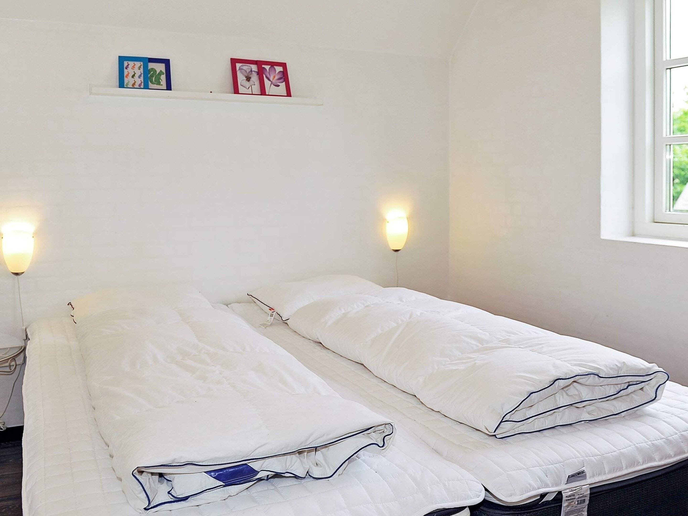 A simple room with two beds, a shelf with pictures, and wall-mounted lights.
