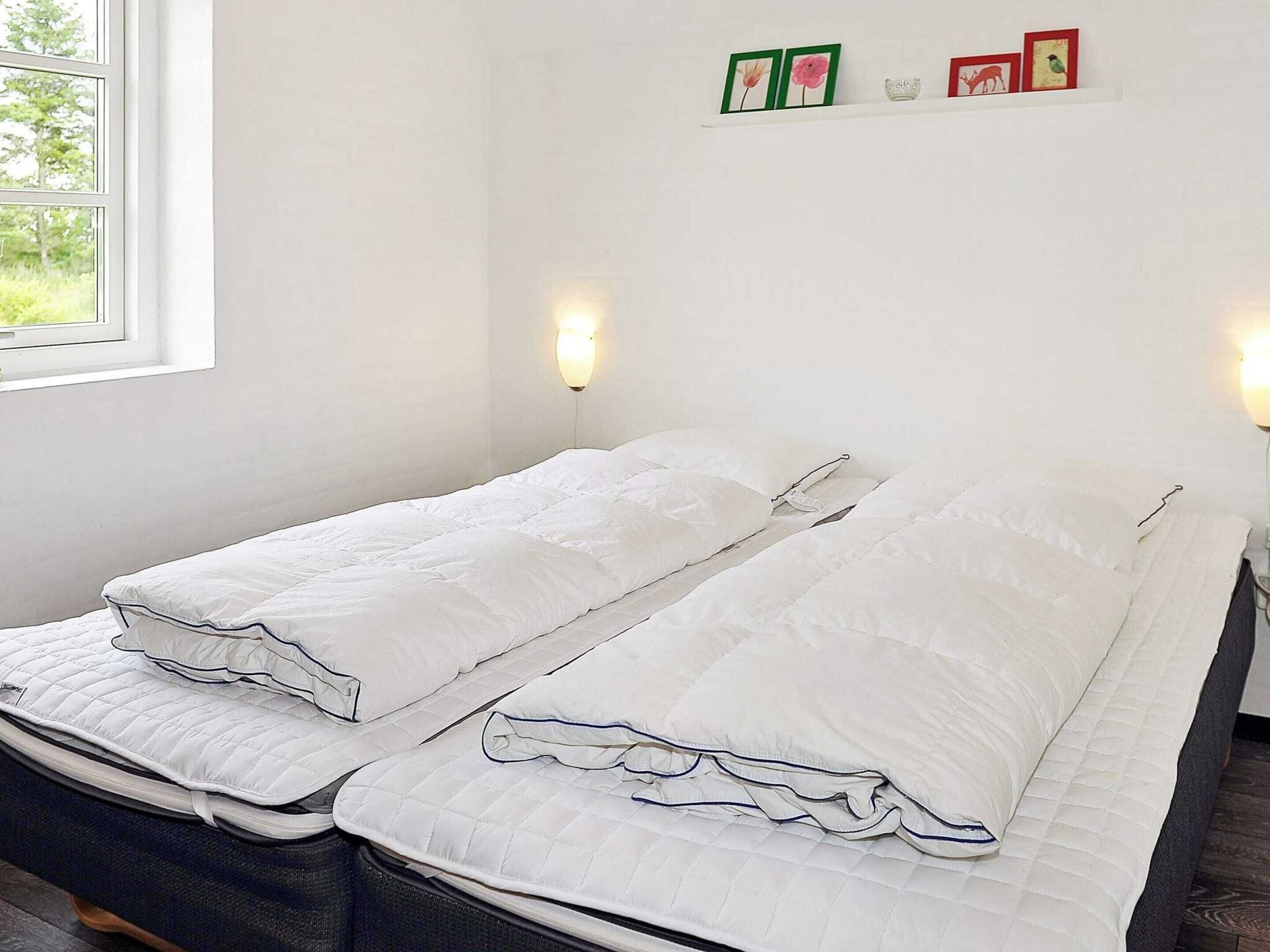 A double bed with white bedding, two wall-mounted light fixtures, and a shelf with framed pictures.