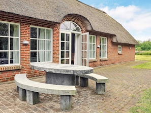 A brick building with a thatched roof, large windows, and a circular stone bench. - Holiday Home in Ulfborg (Ulfborg)