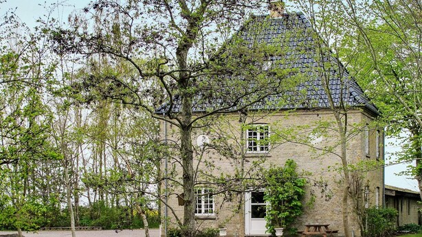 A stone building with a tiled roof, a white bench, and a small pond. - Historic Water Tower Retreat-by Traum (Dannemare)
