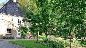 A house with a paved driveway leading to a white door, surrounded by lush greenery and a well-maintained lawn. - Historic Water Tower Retreat-by Traum (Dannemare)