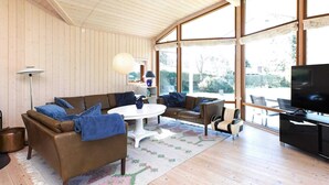 A modern living room with wooden walls and large windows, furnished with sofas and a coffee table. - Holiday Home in VÃ¦ggerlÃ¸se (Vaeggerlose)