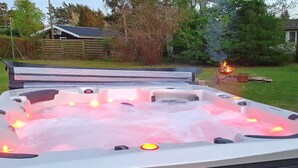 A hot tub with a built-in fire feature, surrounded by a wooden deck and a grassy yard. - Holiday Home in VÃ¦ggerlÃ¸se (Vaeggerlose)
