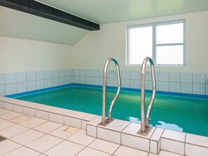 Ein Hallenbad mit zwei Metallleitern, gefliesten Wänden und einem Fenster.
