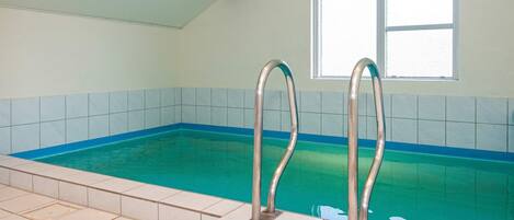 An indoor swimming pool with two metal ladders, tiled walls, and a window.