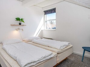 A small, bright room with two beds, a window, a plant, and a blue chair.