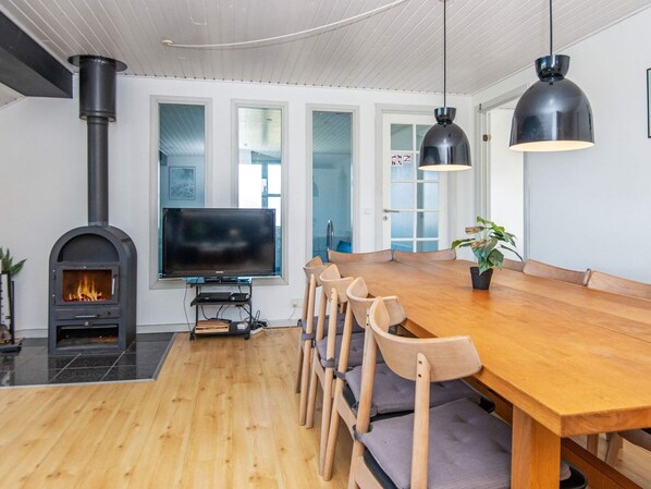 A modern kitchen with a wood-burning stove, a large dining table, and a TV.