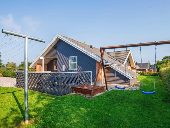 A residential house with a sloped roof, a wooden deck, and a swing set in the yard. - Holiday Home in Juelsminde (Horsens)