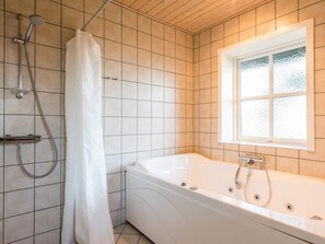 Une salle de bain moderne équipée d’une baignoire, d’une douche et d’une fenêtre laissant entrer la lumière naturelle.