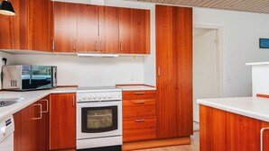A compact kitchen with wooden cabinets, a microwave, and a stove. - 4 Person Holiday Home in Norre Nebel (Norre Nebel)