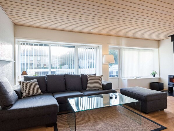 A modern living room with a sectional sofa, a glass coffee table, and a fireplace. - 4 Person Holiday Home in Norre Nebel (Norre Nebel)