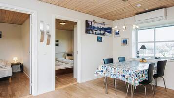 Ein Zimmer mit Holzbalkendecke, einem Bett mit Nachttisch, einem Esstisch mit Stühlen und einem Fenster mit Blick.