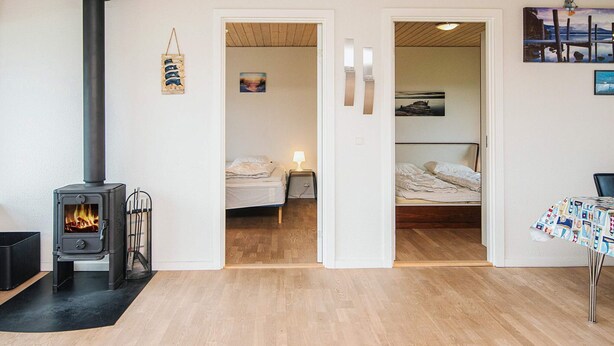 A cozy room with a wood-burning stove, a bed, a table with a tablecloth, and a painting on the wall. - 4 Person Holiday Home in Norre Nebel (Norre Nebel)