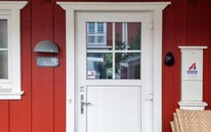 Un edificio rojo con puerta blanca, un buzón y un letrero con una 'A' roja en la pared.