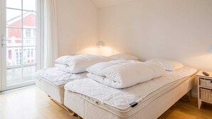 A bedroom with a large bed, a bedside table, and a window with a view of buildings. - 4 Star Holiday Home in Blavand (Blavand)