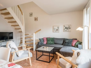 Un salon avec un escalier, un canapé, une table basse et un téléviseur.