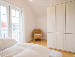 A bedroom with a bed, a wicker chair, and a white wardrobe. - 4 Star Holiday Home in Blavand (Blavand)