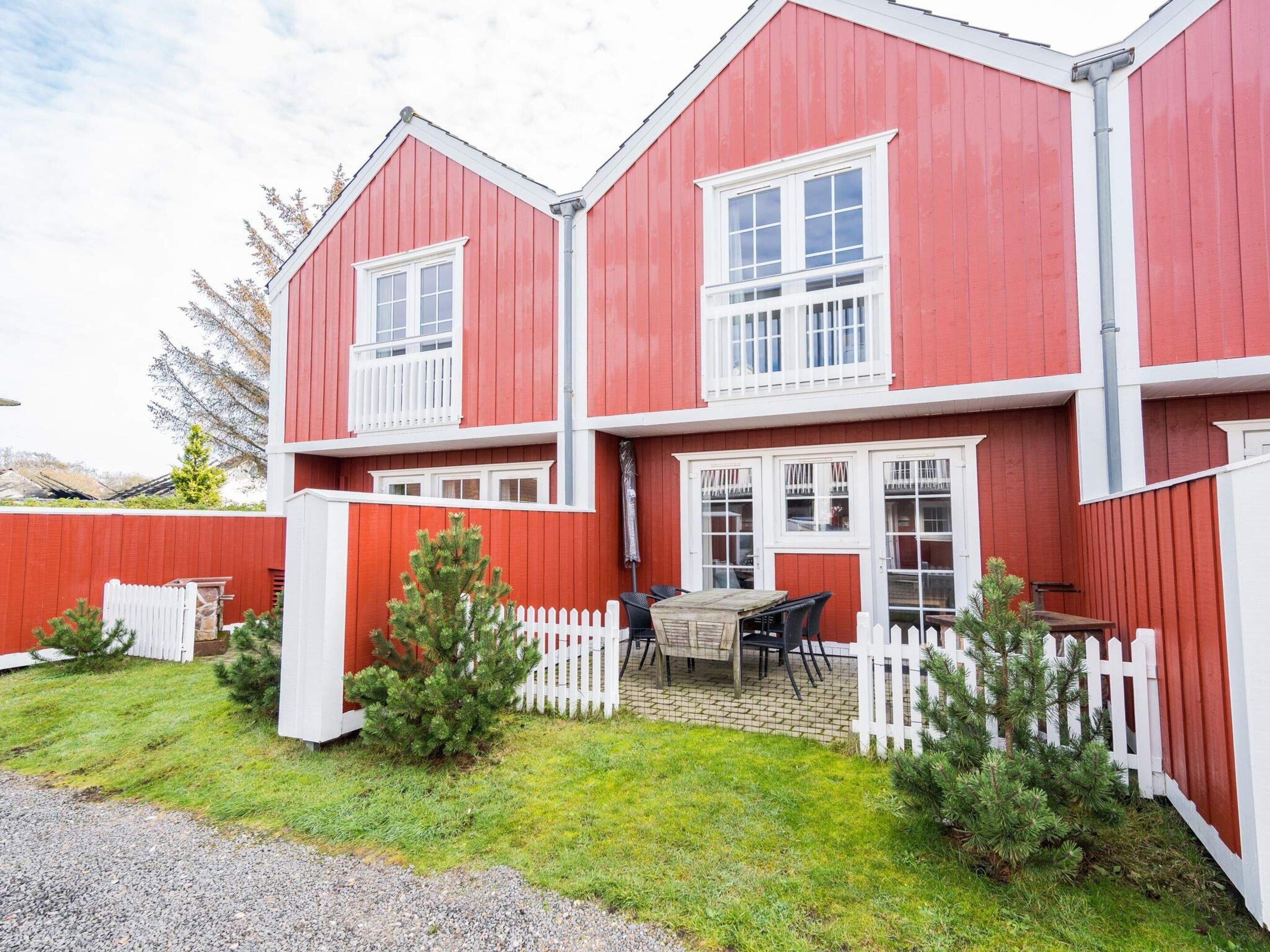 A two-story red building with white trim, a fenced yard, and a small patio with outdoor furniture.