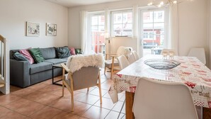 A cozy living room with a grey sofa, a fluffy chair, and a dining table with a patterned tablecloth. - 4 Star Holiday Home in Blavand (Blavand)